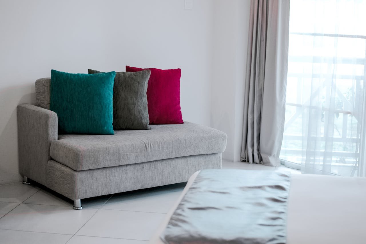 our-journey-03 Simple modern interior featuring a grey sofa with vibrant colored cushions in a bright room.